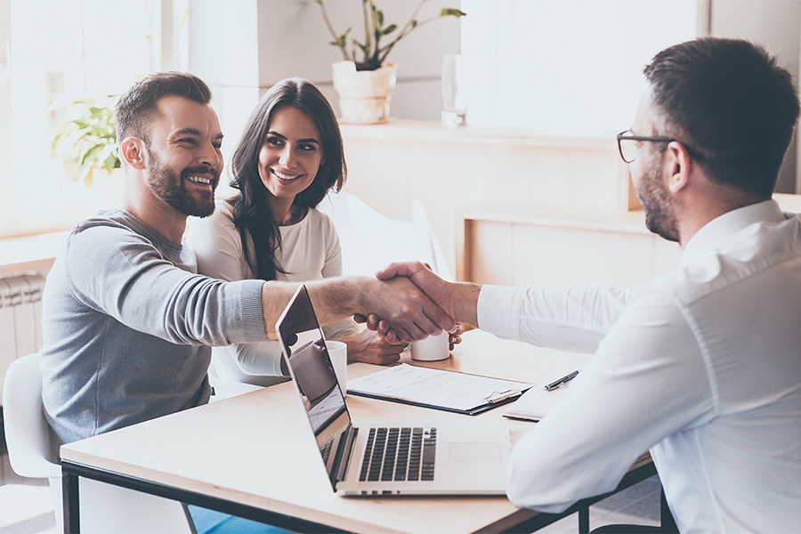 Client Center - Smiling Couple Shaking Hands With Their Insurance Agent In Office