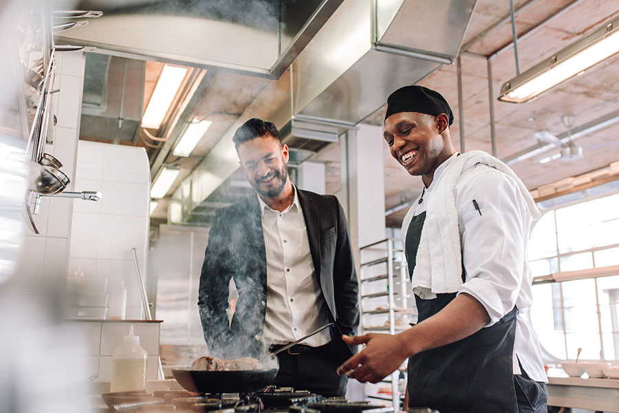 Specialized Business Insurance - Smiling Young Chef Cooking For Restaurant Owner